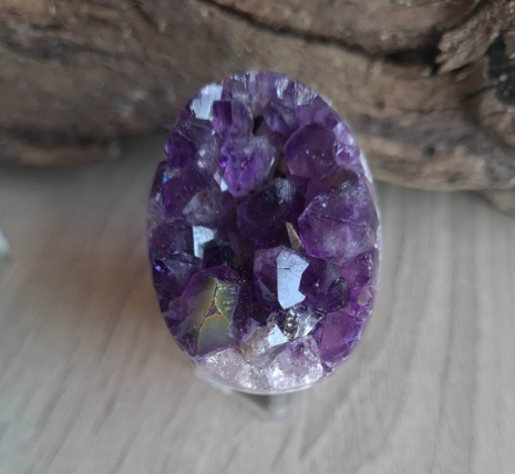 An egg-shaped cluster of amethyst crystals with a deep purple color and a transparent central area, placed on a wooden surface.