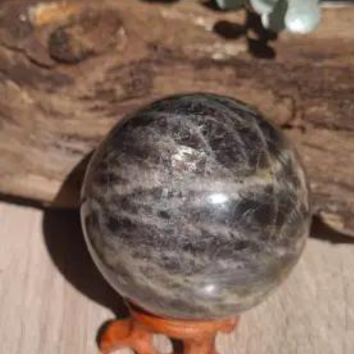 A polished black moonstone sphere displayed on a small wooden stand, with a blurred background.